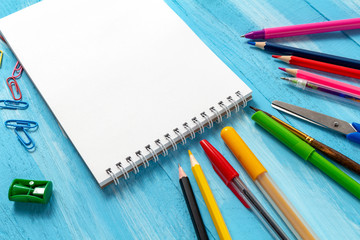Notebook blank pages with colorful pencils, markers and pens composition Back to school concept with stationery office supplies on a blue wooden background with copy space close-up top view