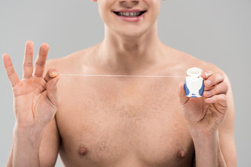 cropped view of naked young man holding dental floss isolated on grey