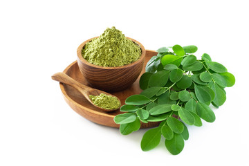 Moringa powder in wooden bowl with original fresh Moringa leaves isolated on white background.