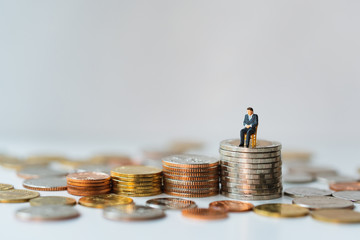 Miniature people, businessman sitting on stack coins using as business and financial concept