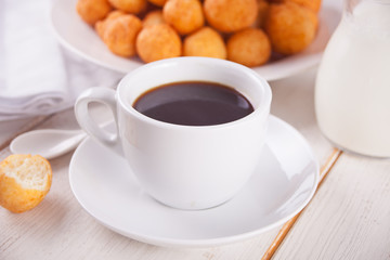Cup of coffee with small balls of freshly baked homemade cottage cheese doughnuts in a plate on a background.