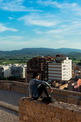 Back view of young man looking at city from castle rooftop