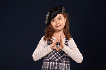 Stylish brunette kid is posing in studio on a black background. Children's fashion.