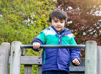 Cute little boy playing slide at the playground, Adorable kid standing on the slide tree and looking down with smiling face, Active child playing outdoors in the sunny day in spring