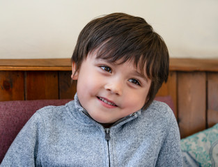 Portrait of Happy boy looking out  with smiling face, Head shot caucasian child sitting on sofa relaxing at home, Close up face of kid laughing,