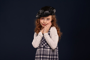 Stylish brunette kid is posing in studio on a black background. Children's fashion.