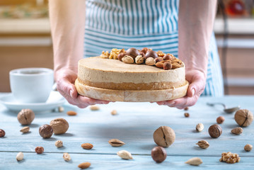 Nutty cheesecake with topping of walnut, almond, hazelnut. Confectioner in a blue apron decorated homemade dessert.