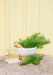Bunch of herbal plant Equisetum arvense the field horsetail or common horsetail in white mortar and tea infusion next to it, yellow background with copy space. Herbal remedy concept.
