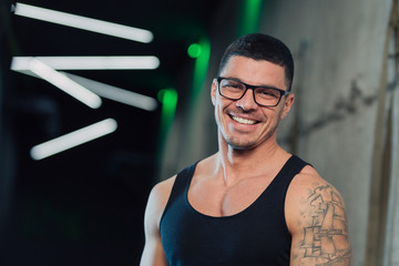 Young strong man in gym in glasses and tanktop smiling