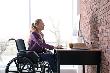 Woman in wheelchair working with computer at table indoors