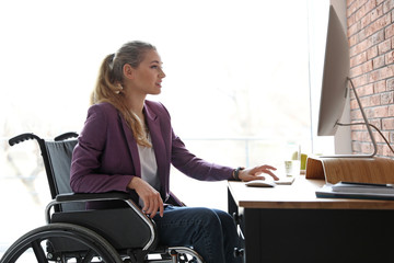 Woman in wheelchair working with computer at table indoors