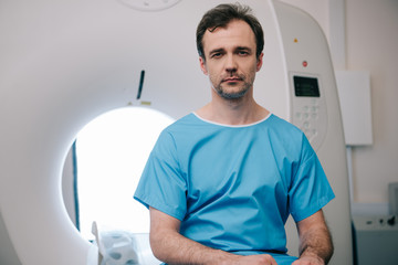 thoughtful man sitting on ct scanner bed and looking at camera
