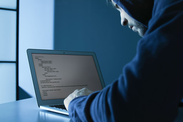 Man using laptop in dark room. Criminal offence