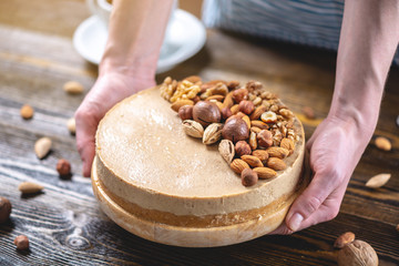 Nutty caramel cheesecake cake with topping of walnut, almond, hazelnut and macadamia on a dark wooden background.