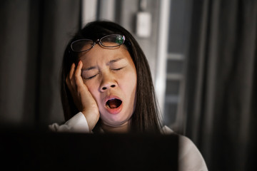 tired Asian female working late at night yawning in front of computer laptop  