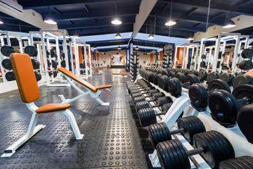 New fitness machines and dumbbells in modern gym interior