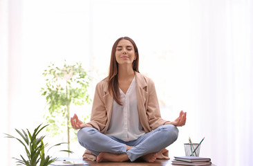 Young businesswoman meditating at workplace. Zen concept - obrazy, fototapety, plakaty