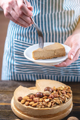 Nutty cheesecake on a dark wooden background. Confectioner in a blue apron holding a piece of nut cake