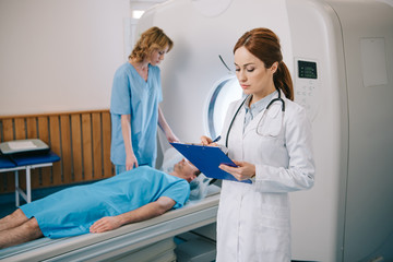 nurse preparing patient for mri scanning while radiologist writing on clipboard