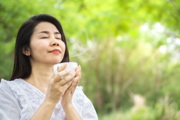 beautiful Asian woman enjoying smell  hot coffee cup relaxing in nature green park