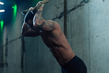 Young strong man in gym doing suspended exercises with straps in the gym