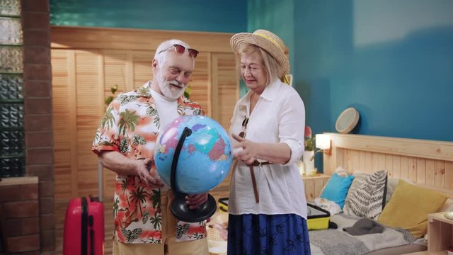 Happy senior couple looking hold globe talk going on holiday senior suitcase together caucasian holiday bag elderly family girl home mature older pensioner tourism travel trip slow motion