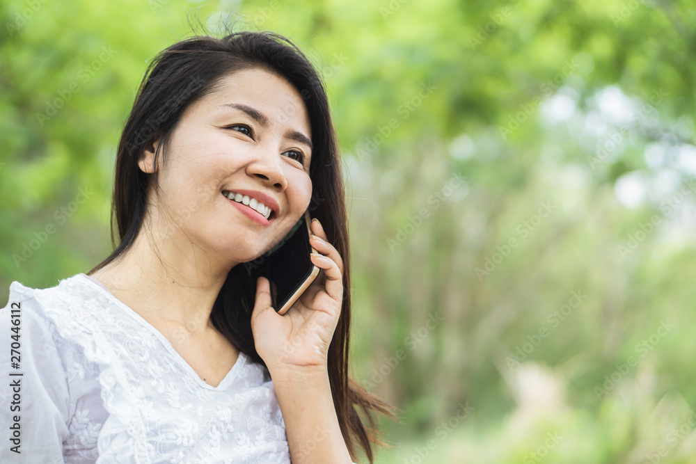 Wall mural asian woman talking on smart phone in nature park with smiling face