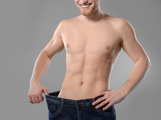 Fototapeta premium Young man with slim body in old big size jeans on grey background, closeup