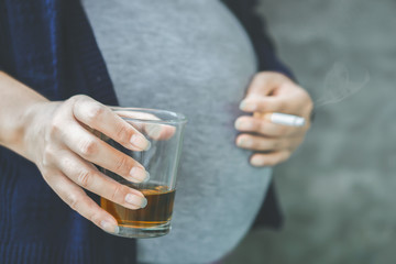 careless pregnant Asian woman drinking glass of alcohol another hand smoking cigarette 