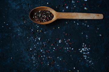 Colored pepper and salt on a wooden spoon isolated on black table background. Copy space