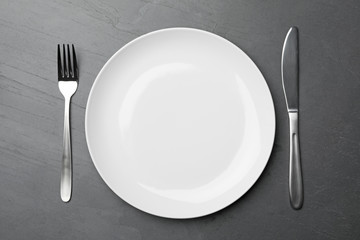 Stylish ceramic plate and cutlery on dark background, flat lay