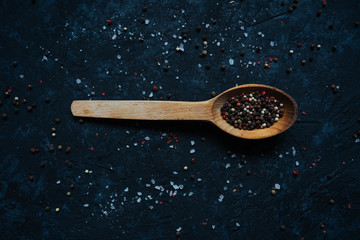 Colored pepper and salt on a wooden spoon isolated on black table background. Copy space
