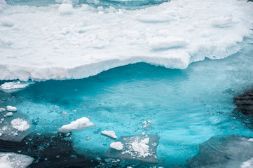 Close up of an ice berg shows ice is breaking away and visible beneath sea is the bulk of the berg - Image