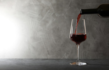 Pouring red wine from bottle into glass on table. Space for text