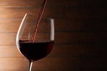 Pouring red wine into glass on blurred background. Space for text