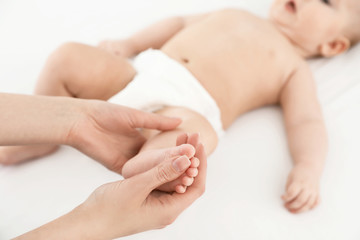 Mother and her cute child on white bed, closeup. Baby massage and exercises