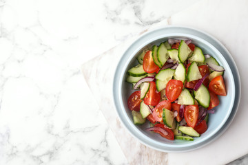 Bowl of vegetarian salad with cucumber, tomato and onion on marble background, top view. Space for text