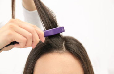 Hairdresser using modern flat iron to style client's hair in salon, closeup