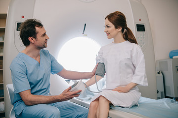 Obraz premium handsome doctor measuring patients blood pressure with tonometer while sitting at mri scanner