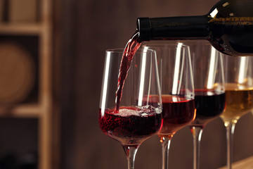 Pouring wine from bottle into glass in cellar, closeup