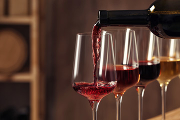 Pouring wine from bottle into glass in cellar, closeup