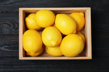 Wooden crate full of fresh lemons on dark background, top view