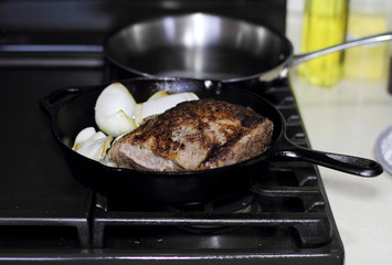 Sirloin steak frying in a cast iron pan with onions on the stove top.