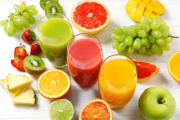 Glasses with different juices and fresh fruits on wooden table