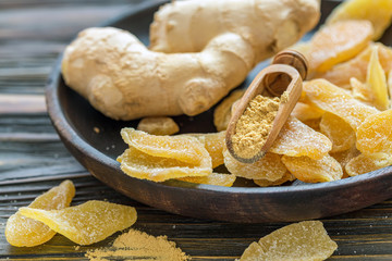Ginger root and candied ginger on a wooden plate.
