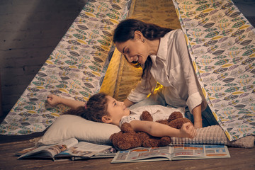 Mother and her daughter are in a teepee tent with some pillows. Happy family.