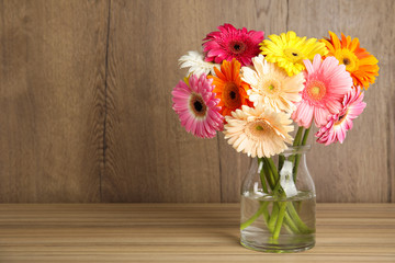 Bouquet of beautiful bright gerbera flowers in glass vase on table against wooden background. Space for text