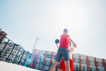 Two Caucasian friends wearing red sports equpment playing basketballs outdoors on a sunny day while they dribble and push each other.