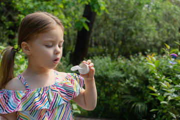 Cute little girl is blowing a soap bubbles in the garden