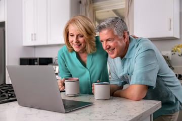 Happy senior couple retired at home enjoying the internet together, smiling laughing and cheerful.